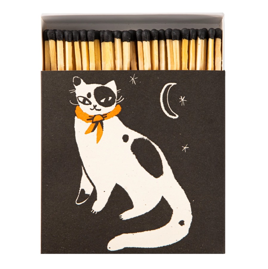 A black matchbox printed with a white cat in an orange neckerchief, under a crescent moon